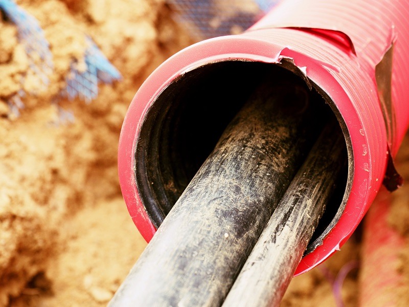 Fibre optic cabling being laid in the ground in a red, plastic tube surrounded by soil.