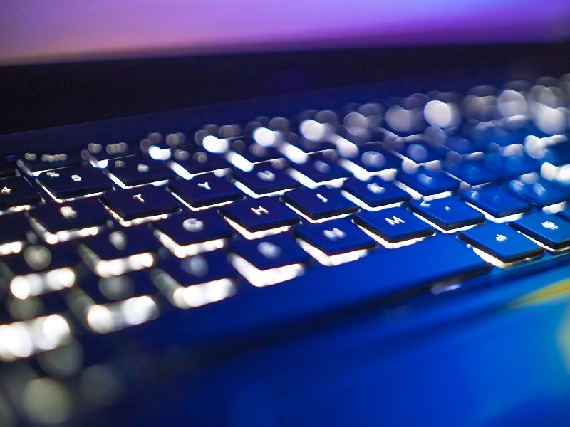 close-up of a backlit keyboard in a dark room with purple tones.