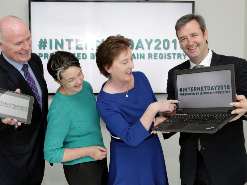 Three people point to a computer being held by a man in a suit.