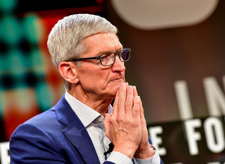 Apple CEO Tim Cook wearing a blue suit, holding his hands together under his chin.