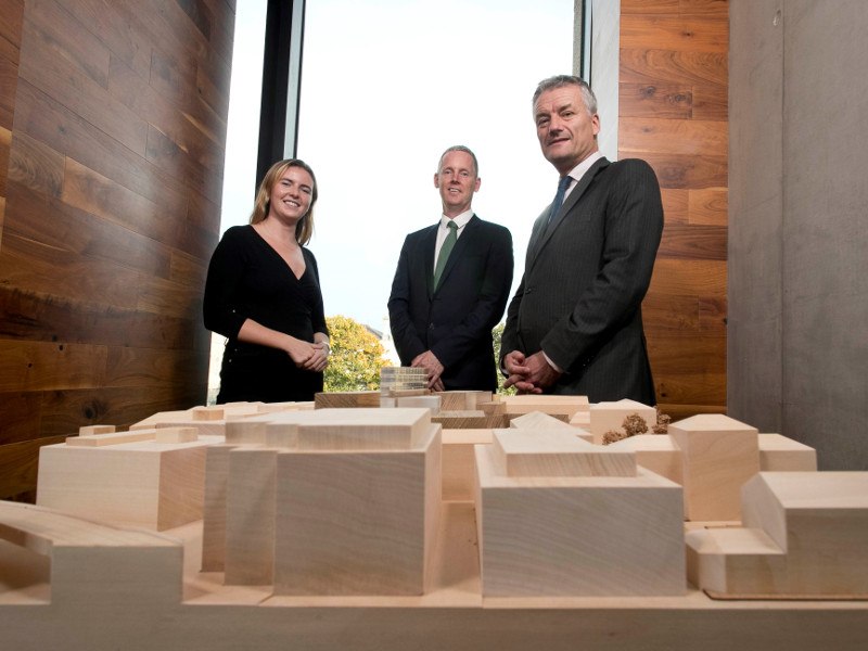 A woman and two men stand over a model of Trinity College Dublin.