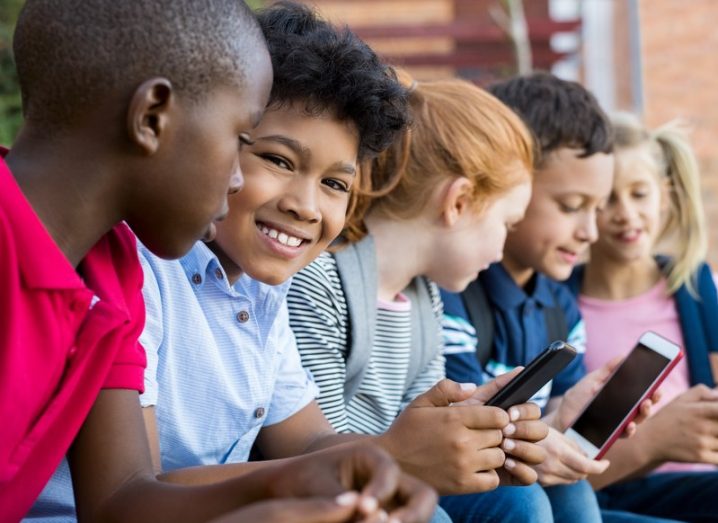 A group of diverse children using their smartphones outdoors.