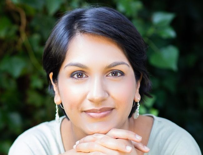 Angela Saini smiling, resting her chin on her hands.