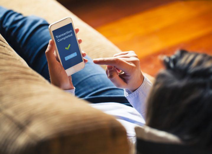 Woman reclining on couch completes a transaction on her smartphone.