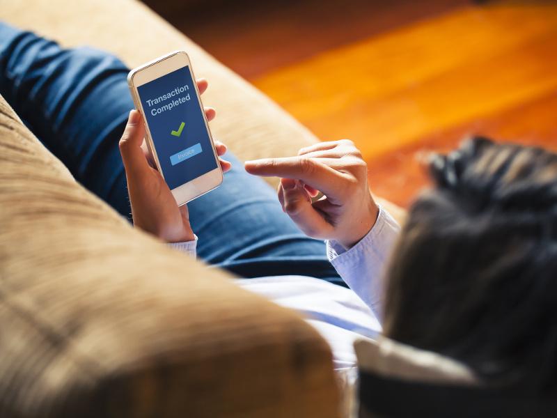 Woman reclining on couch completes a transaction on her smartphone.