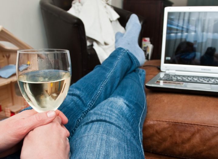 Woman watching Netflix on a laptop with a glass of wine.