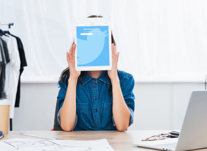 woman in denim shirt holding tablet with twitter open on it, hiding her face.