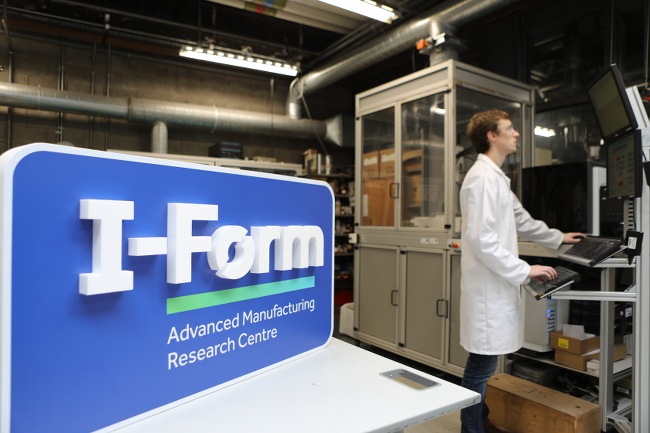 A three-dimensional I-Form sign with a scientist working at a standing computer in the background.