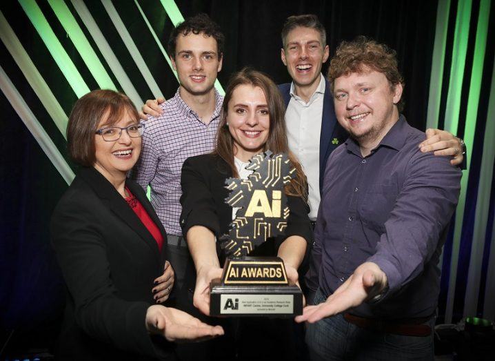 AI Award winners holding one of the trophies against a black and green striped background.