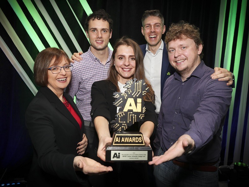 AI Award winners holding one of the trophies against a black and green striped background.