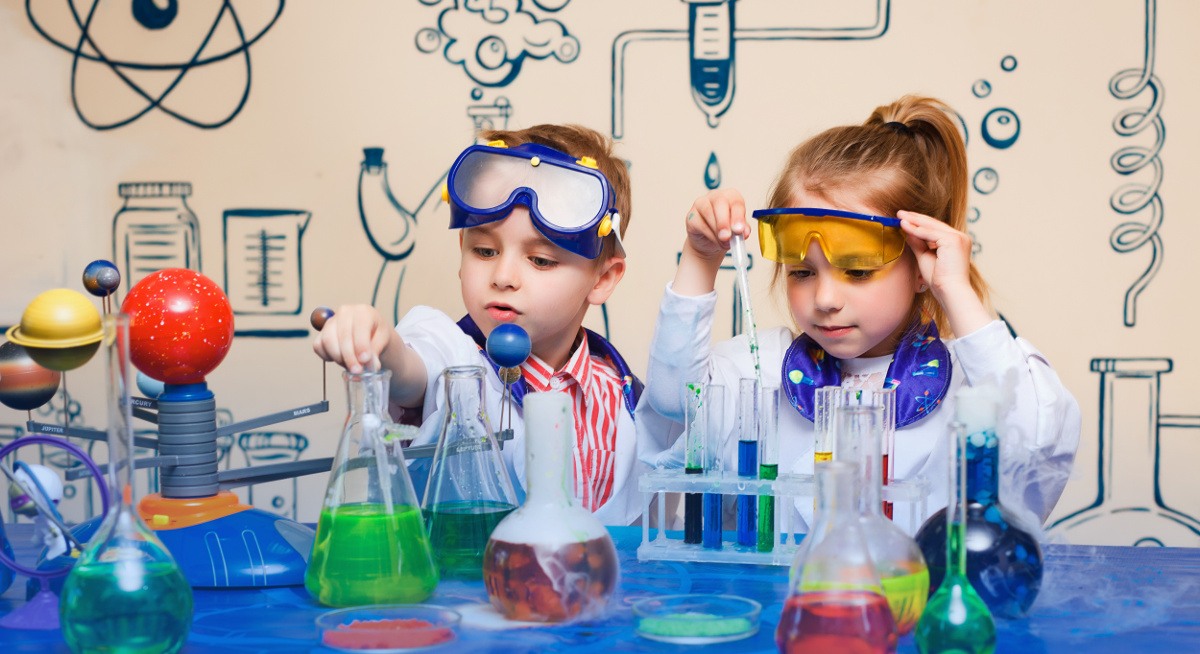 A young boy and girl dressed as scientists, playing with an assortment of beakers, dreaming of a science career.