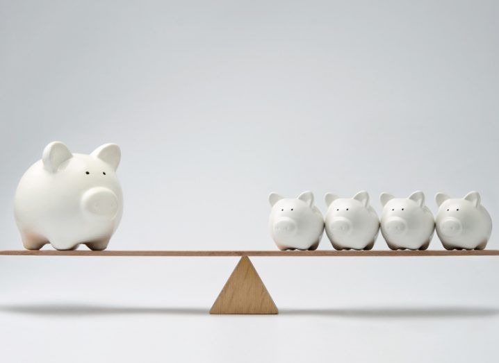 A see-saw balanced equally with one large white ceramic piggy bank on one end and four smaller piggy banks on the other.