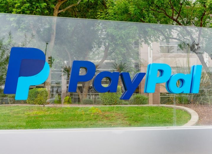 The PayPal logo on a glass panel outside an office in Arizona, with trees in the background.