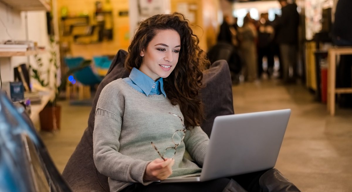 Beautiful young woman working on laptop and smiling while sitting inside looking at the top freelancer skills.