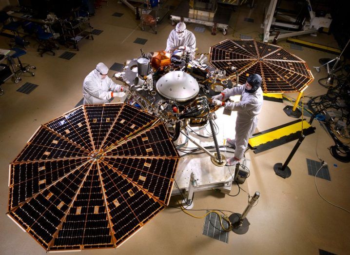 Engineers in white jumpsuits working on the InSight lander with solar arrays open.