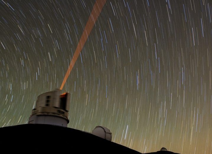 Time-lapse shot of moving stars with a observatory emitting a laser beam in the foreground.