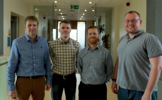 four men wearing shirts standing in hallway.