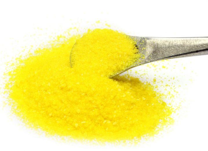 Flourescent yellow powder poured from a small metal spoon against a white background.