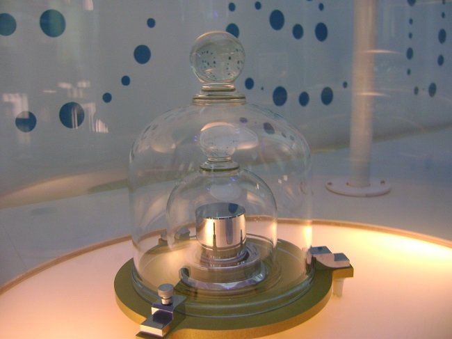 A replica of the definitive kilogram weight held within a bulb-like glass jar.