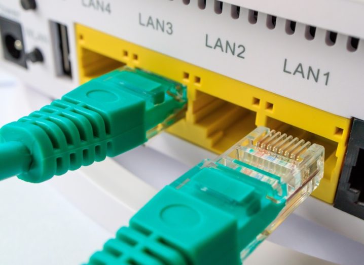 Green ethernet cables being plugged into a Wi-Fi router.