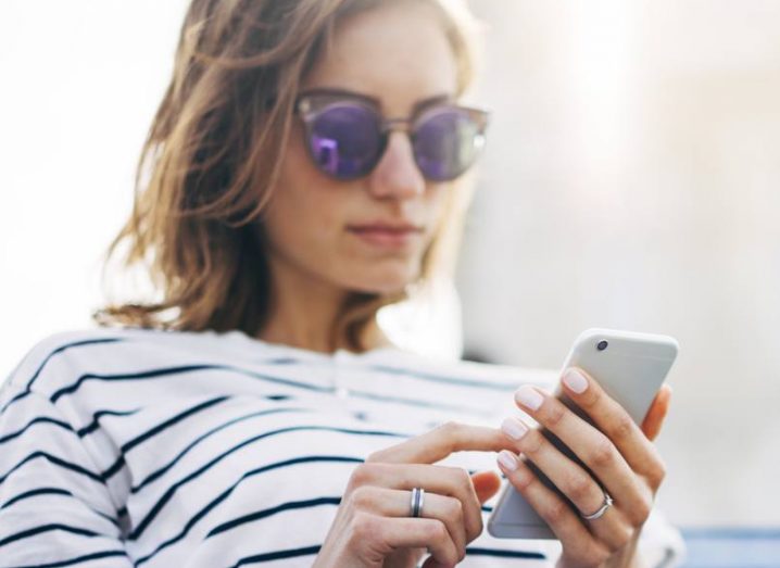 A young woman wearing a striped shirt and sunglasses using a smartphone.