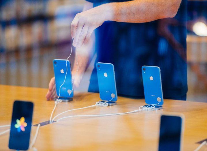 An Apple Store assistant displays blue-coloured Apple XR devices.