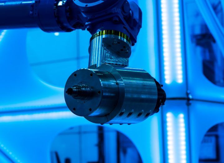Robotic manufacturing arm above a shiny, blue reflective surface.