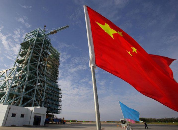 China flag waving in the foreground with a launch facility in the background.