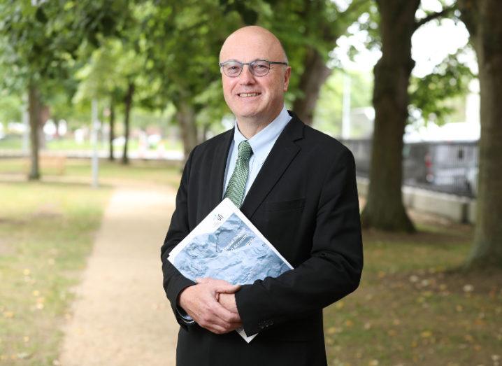 A man in a suit and glasses stands in a park holding the SFI 2017 Annual Report in his hands.