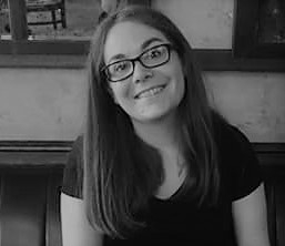 black and white picture of smiling young woman with long dark hair wearing glasses and dark tshirt.