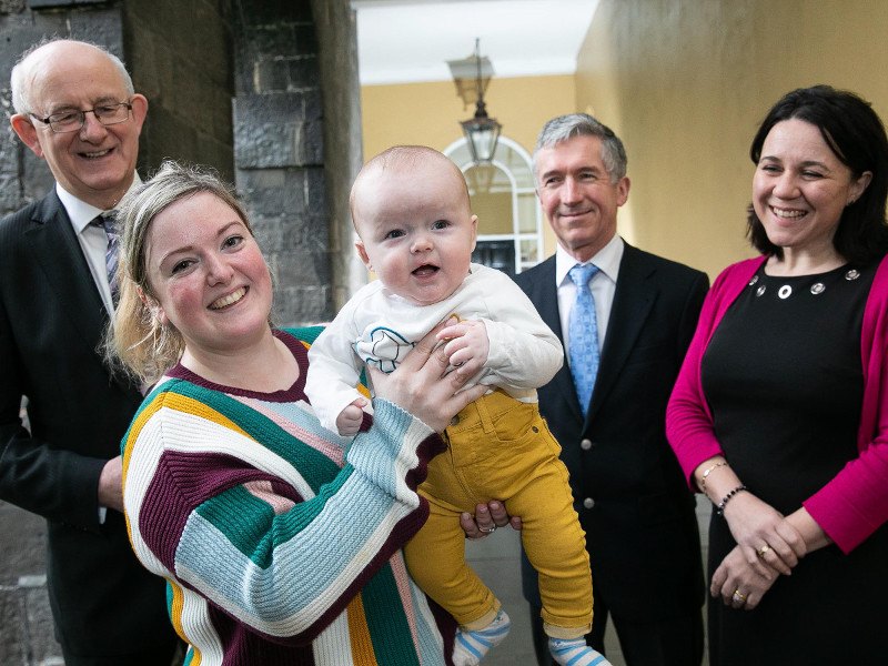 woman holding up her smilingbaby son beside two male and one female health representatives.