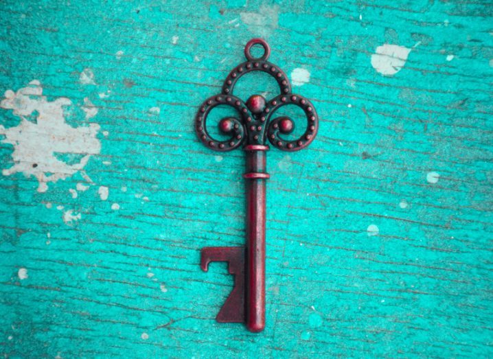 old-fashioned ornate brass key on teal wood background.