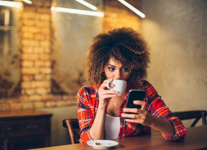 Young woman scans her smartphone while drinking a coffee.