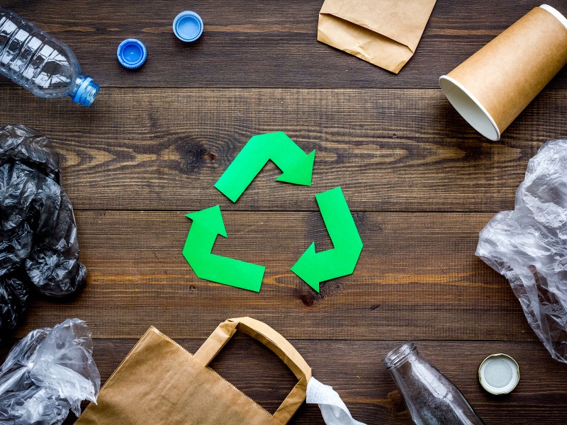 Discarded bags, bottles and disposable cups surround a paper cut-out recycling logo.