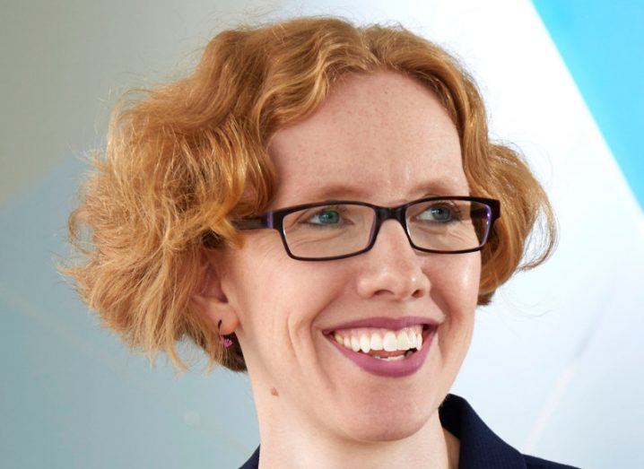 A smiling woman with short red hair and glasses.