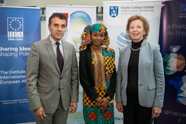 A man in a grey suit, a woman in a colourful patterned dress and headpiece and an older woman in a blazer pose together.