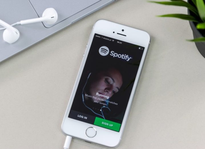 An iPhone SE smartphone with the Spotify app home screen on display, resting on a white desk.