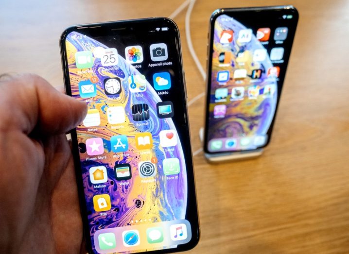 Hand holding an iPhone XS device with app icons visible on display.