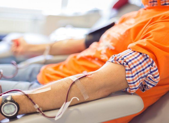A person wearing an orange jumper with their sleeve up while hooked up to a blood donation machine.