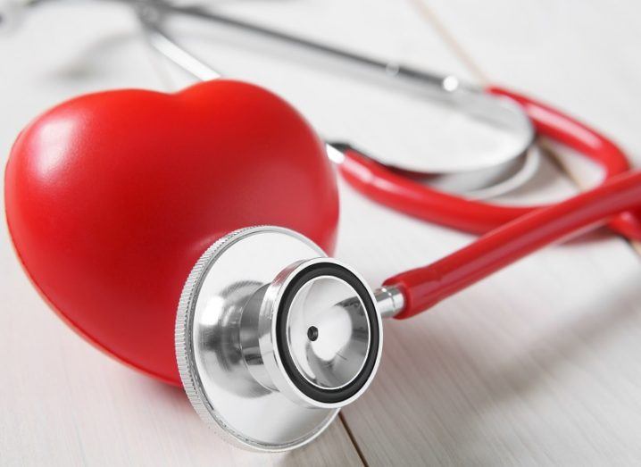 Close-up of a large, rubber heart with a stethoscope leaning against it on a wooden table.