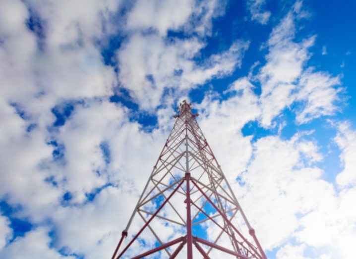 Inside view of telecommunication tower with panel antennas and radio antennas and satellite dishes for mobile communications 2G, 3G, 4G, 5G with red fence around tower against blue sky with clouds.