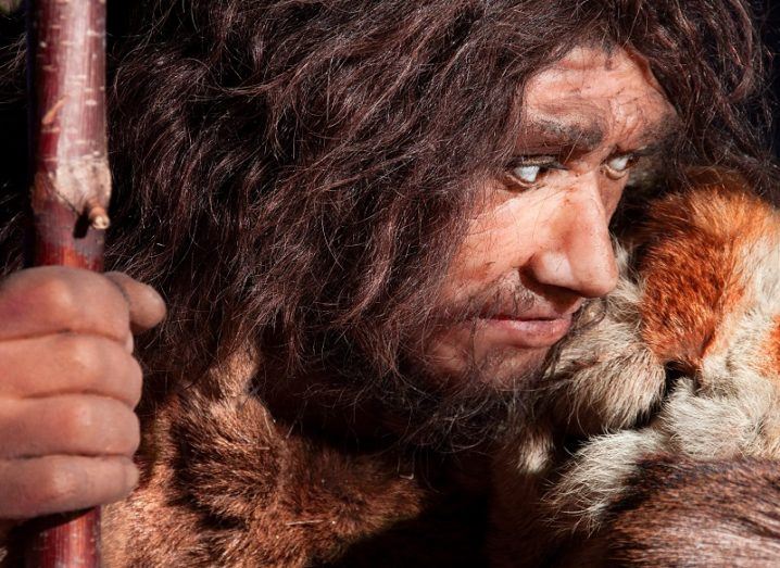 Close-up of a Neanderthal waxwork man with long hair and beard holding a spear.