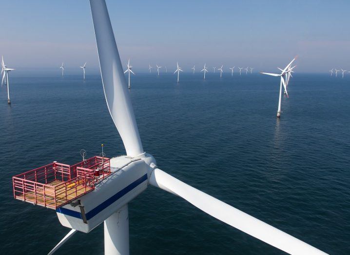 Closeup of the rear of an offshore wind turbine with many other turbines shown in the distance.