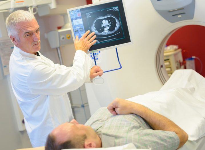 Man undergoing body scan while a doctor discusses his diagnosis with a doctor using a screen.