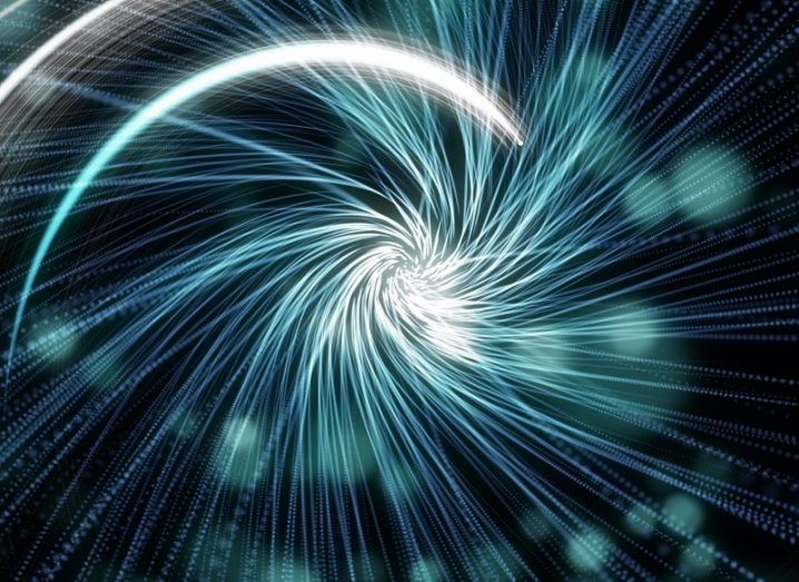 Abstract image of travelling through time into a light blue spiral against a black background with light blue spots.