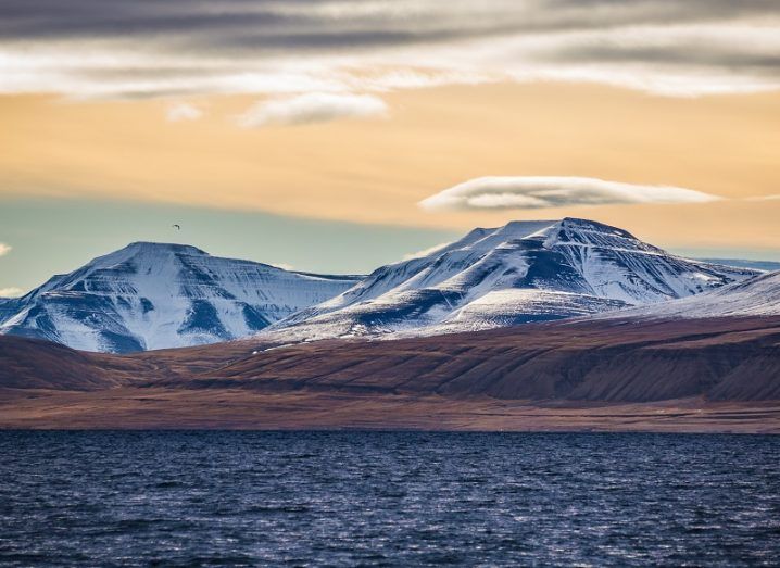 The ocean, desolate land and icy mountains of Svalbard against backdrop of a setting sun.
