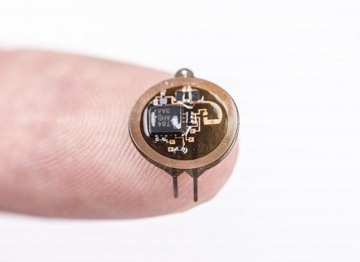 The tiny circular implant device being held on the end of a person's finger.