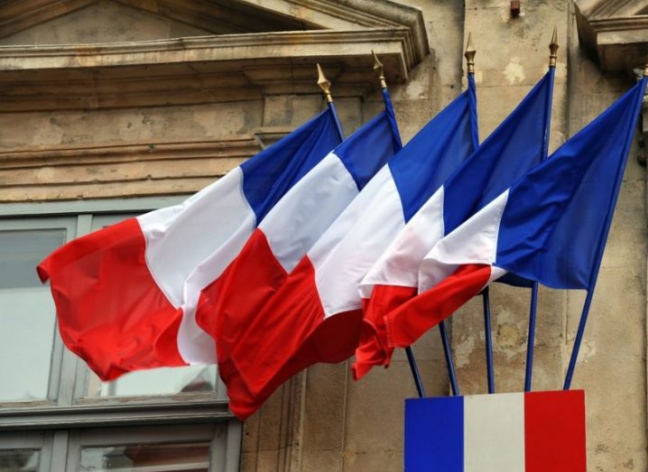 Five French flags waving outside an old stone building.