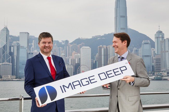 Two men in suits hold a sign with Hong Kong in background.