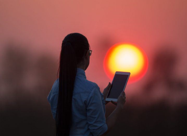 Woman holding a tablet computer in a field at sunset.